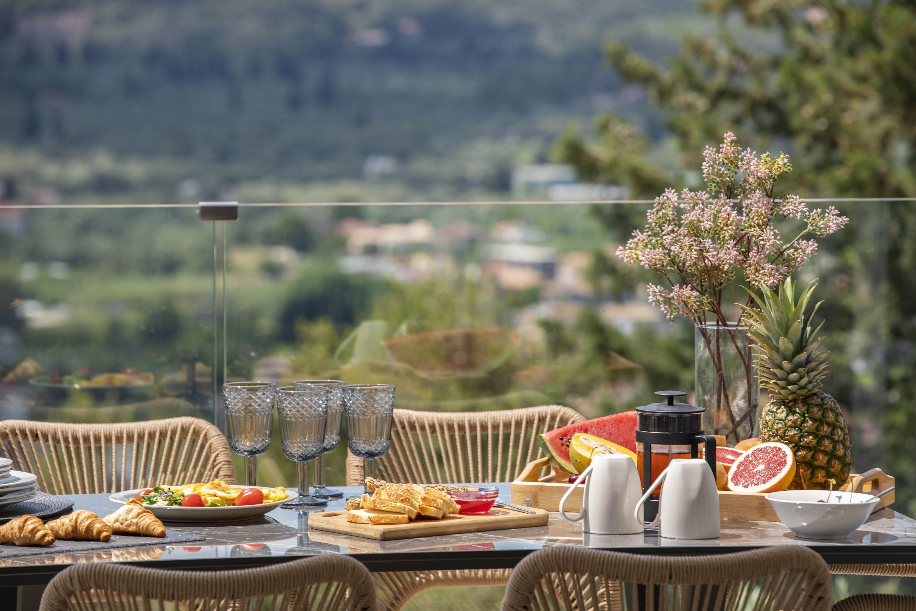 A table set with breakfast items, a pineapple, and a view of a lush landscape.