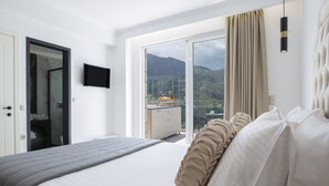 Ett hotellrum med en säng, en tv och en skjutdörr i glas som leder ut till en balkong med utsikt över bergen.