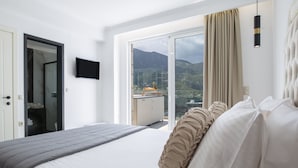 A hotel room with a bed, a television, a sliding glass door leading to a balcony with a mountain view. - Villa Cristina Lefkada (Nydri)