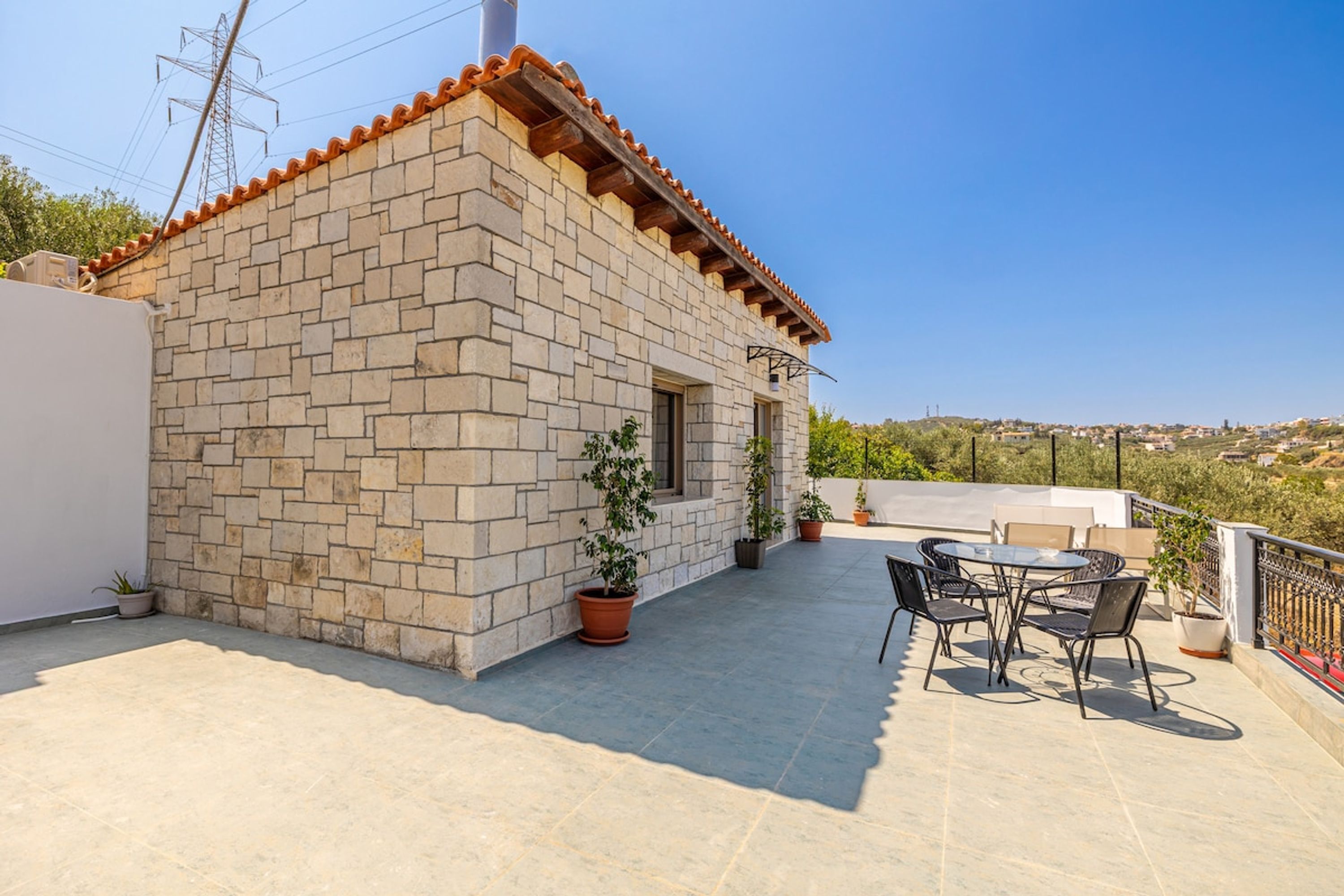 Un edificio de piedra con techo de tejas, un patio con mesa y sillas, y macetas con plantas.