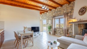 A spacious living area with a stone wall, a fireplace, a dining table, and a sofa. - Elea Home by cretanhouses (Gournes)