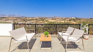 A terrace with a wooden table and two white chairs, a potted plant, and a view of a hilly landscape. - Elea Home by cretanhouses (Gournes)