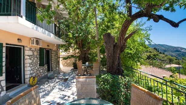 Un edificio in pietra con un balcone, mobili in vimini e un grande albero in un cortile.