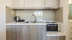 A modern kitchen with wooden cabinets, a stainless steel sink, a kettle, and a built-in oven. - The Walls Apartments | 1 (Iraklio)