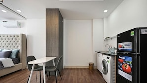 A compact living space with a sofa, a dining table with chairs, a washing machine, and a refrigerator. - M Home Riverside (Ho Chi Minh City)
