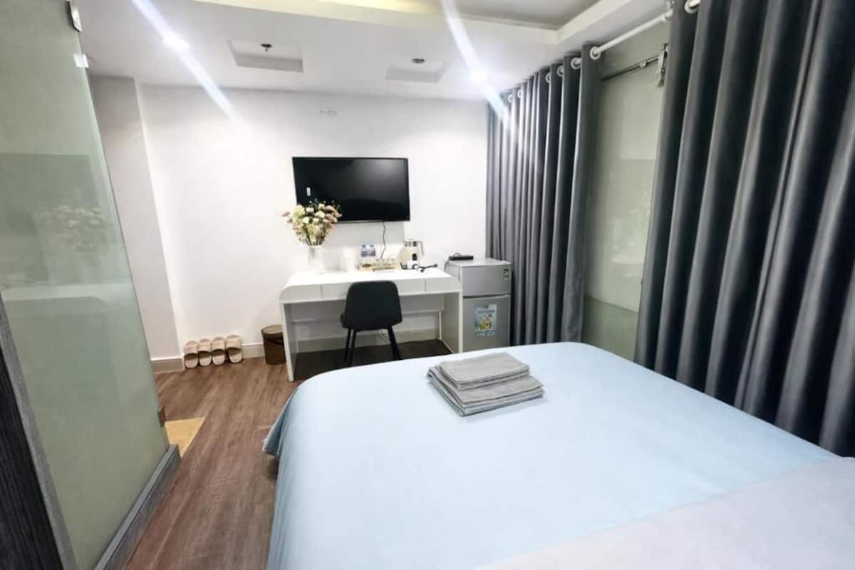 A hotel room with a bed, a desk, a chair, a TV, and a window with curtains.