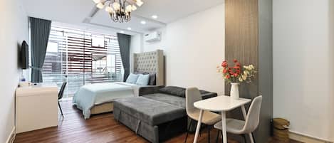 A modern hotel room with a bed, sofa, dining table, and chairs.