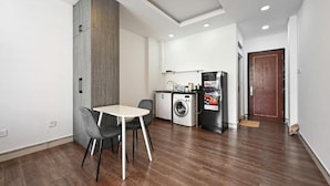 A compact kitchen with a washing machine, a refrigerator, and a dining area with a table and chairs. - M Home Riverside (Ho Chi Minh City)