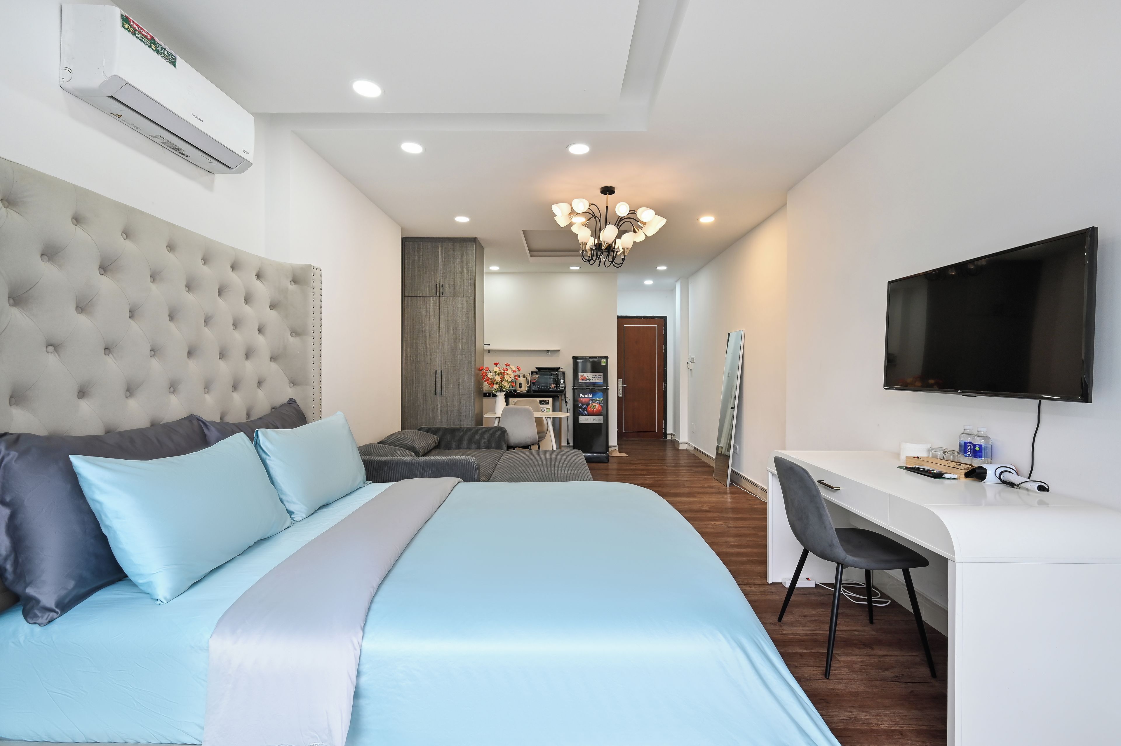 A modern hotel room with a large bed, a desk, a television, and an air conditioning unit.
