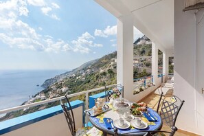 A balcony with a table set for tea, overlooking a coastal town and the sea. - At Nonno Aurelio's: Sea View, Wi-Fi & Air Conditioning (Furore)