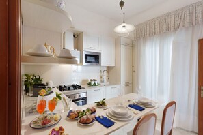 A modern kitchen with white cabinets, a microwave, and a dining area set for a meal. - At Nonno Aurelio's: Sea View, Wi-Fi & Air Conditioning (Furore)