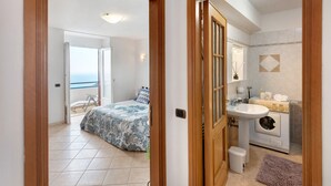 Quarto com cama, banheiro com pia e máquina de lavar, e varanda com vista.