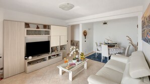 Sala de estar com televisão, sofá, mesa de centro e área de jantar.