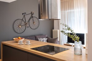 Une cuisine moderne avec un plan de travail en bois, une plaque de cuisson à induction intégrée, un saladier rempli de fruits et un vélo accroché au mur.