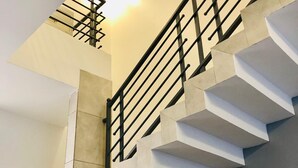 Una escalera moderna con un diseño geométrico, barandilla de metal y una lámpara colgante.
