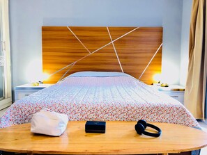 A neatly made bed with a floral-patterned duvet, a bedside table with a lamp, a power strip, and a small box.