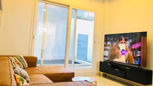 Una sala de estar con un sofá de cuero marrón, un televisor y un ventanal corredera que da a un balcón.