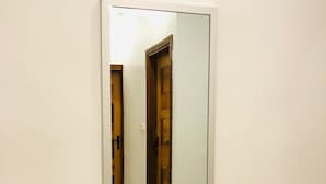 Un pasillo con un espejo grande en la pared, una puerta de madera y un interruptor de luz.