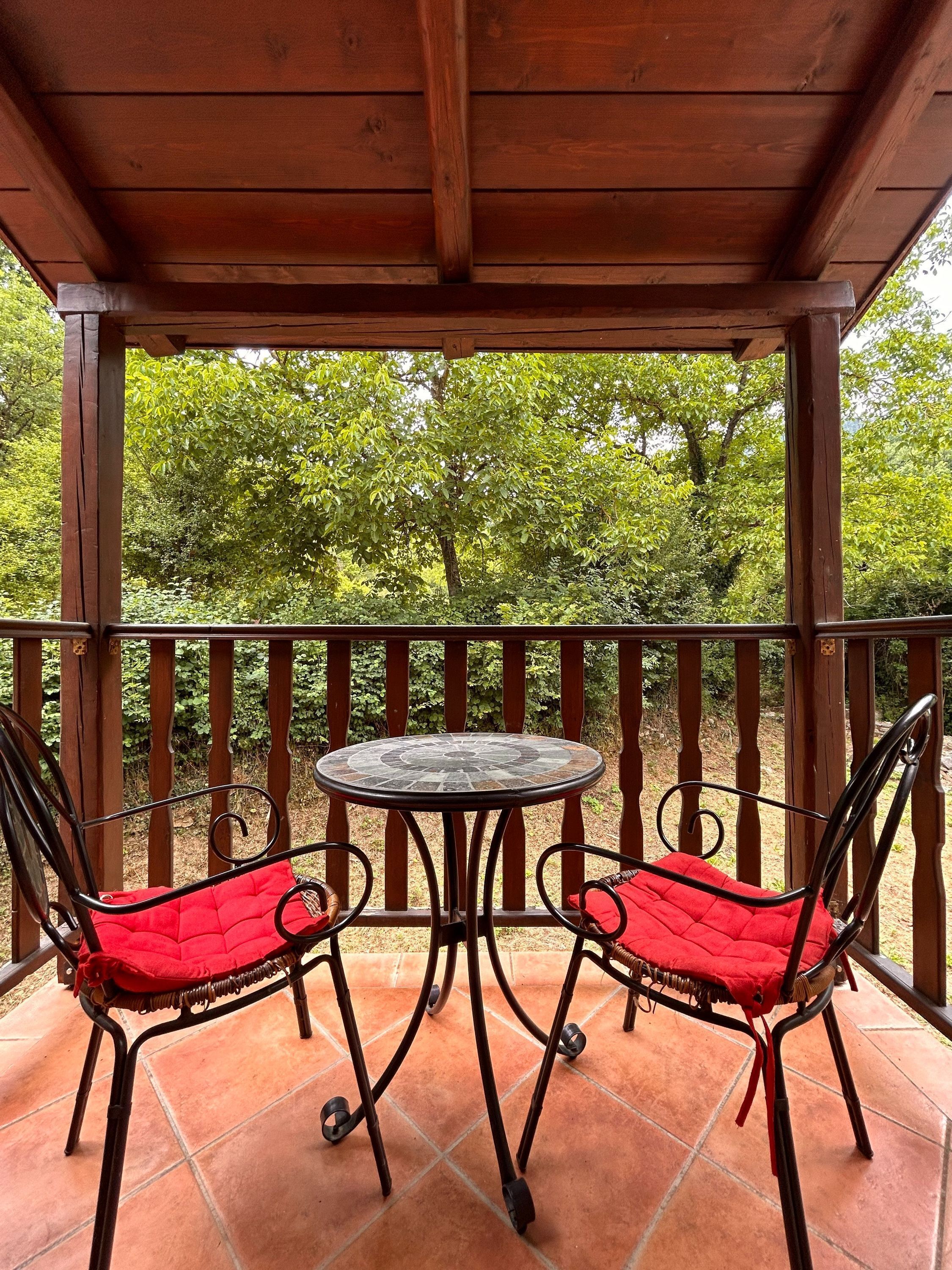 Eine Holzhütte mit einer gefliesten Terrasse, zwei Metallstühle mit roten Kissen und ein kleiner runder Tisch.