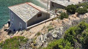 A coastal village with stone buildings, a beach, and a mountainous backdrop.