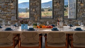 Un comedor con pared de piedra, tres ventanas y una mesa dispuesta para seis personas con sillas.