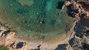 Vista aérea de una zona costera con aguas cristalinas, terreno rocoso y vegetación escasa.