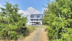 A beachfront property with a wooden walkway leading to a large blue house with a balcony. - Bayfront home with private pool on Slaughter Beach! (Milford)