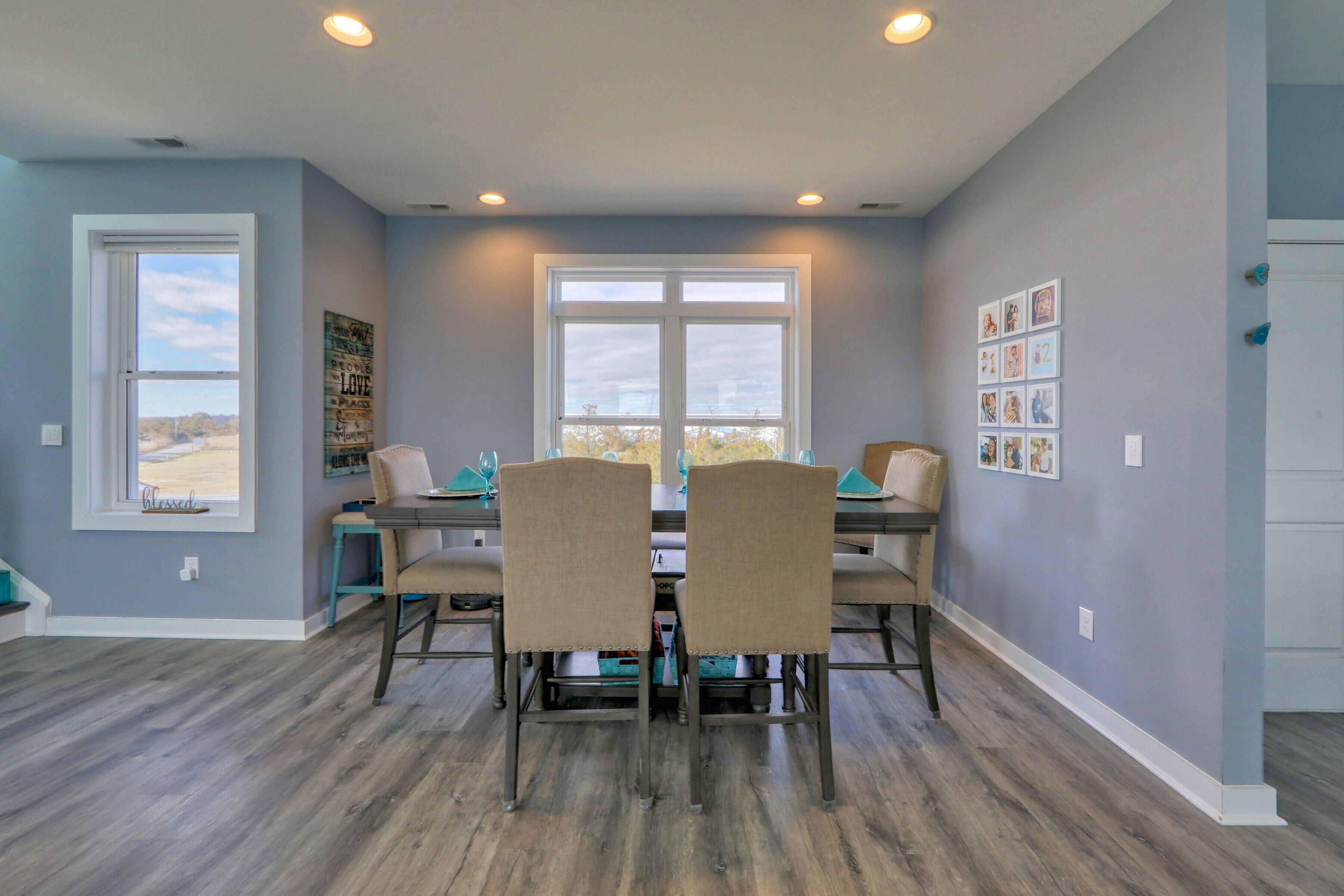 A dining area with a table and chairs, a window with a view, and a wall with framed pictures.