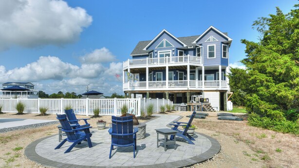 A two-story house with a balcony, outdoor seating area with chairs and tables, and a view of the sky. - Bayfront home with private pool on Slaughter Beach! (Milford)