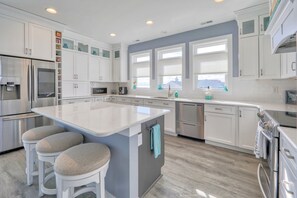 A modern kitchen with white cabinetry, a large island with stools, stainless steel appliances, and a view through the windows.