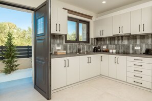Une cuisine moderne avec des meubles blancs, une fenêtre et une vue sur les arbres.