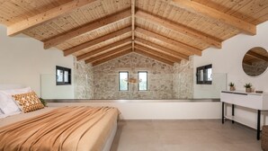 Un dormitorio con pared de piedra, vigas de madera en el techo, una cama con manta estampada, una mesita de noche y un espejo.