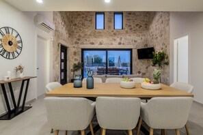 A dining area with a stone wall, a large clock, and a TV mounted on the wall. - Petra Natura Villa I (Laganas)