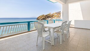 En balkon med et hvidt bord og stole, med udsigt over kysten og bygninger på en skråning.