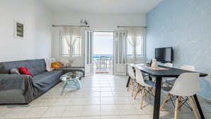 En moderne stue med en grå sofa, et glasbord og et spiseområde med et sort bord og hvide stole.