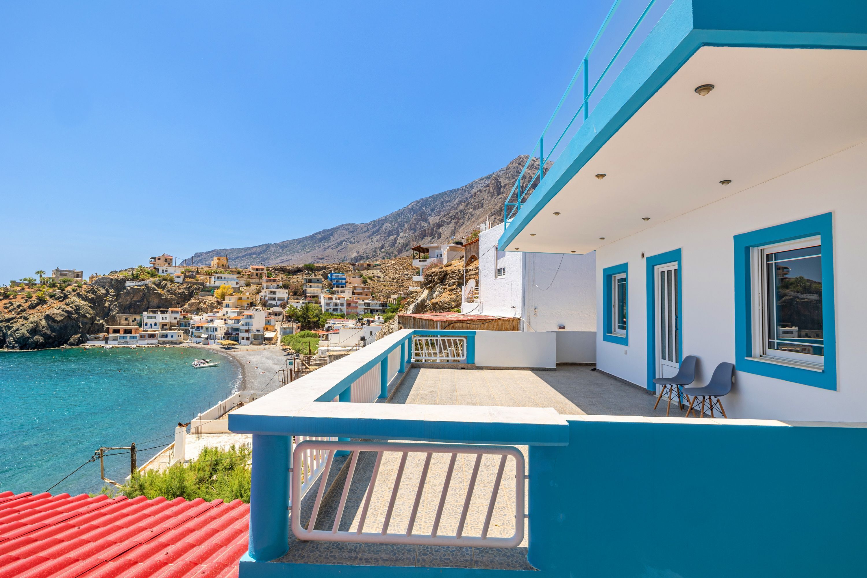 A coastal building with a balcony overlooking a beach and a mountainous backdrop.