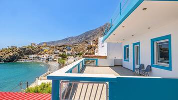 A coastal building with a balcony overlooking a beach and a mountainous backdrop.