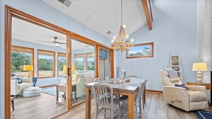 Un comedor espacioso con una mesa y sillas de madera, una araña y ventanas amplias que ofrecen vistas al exterior.