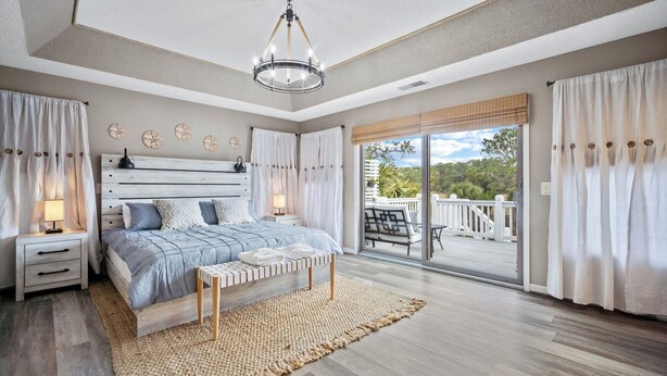Un dormitorio con una cama grande, una mesita de noche, un banco y vistas a un balcón con mobiliario exterior.