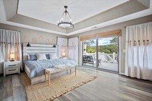 A bedroom with a large bed, a nightstand, a bench, and a view of a balcony with outdoor furniture. - Lake View, Golf Cart Included - 122 Sand Piper (Fripp Island)