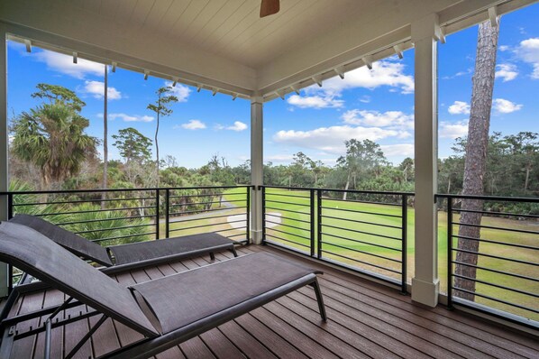 Um espaço ao ar livre coberto com um deck de madeira, duas poltronas de descanso e vista para um campo de golfe.
