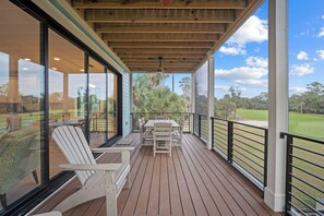 Uma área externa coberta com um deck de madeira, uma mesa com cadeiras e vista para um campo de golfe.