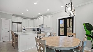 Une cuisine moderne avec des meubles blancs, un îlot central et un coin repas comprenant une table et des chaises en bois.