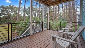 Une véranda couverte avec un plancher en bois, deux fauteuils Adirondack et une vue sur une zone boisée.