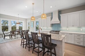 A modern kitchen with white cabinets, a granite countertop, and a large island with bar stools. - Marshfront, Golf Cart Included, Mint Condition - 173 Ocean Creek (Fripp Island)