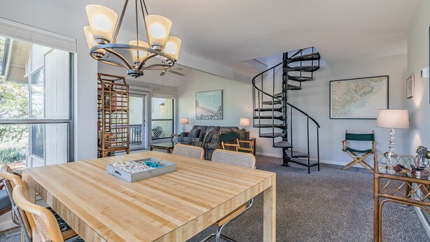 Un amplio salón con una mesa de comedor de madera, una escalera en espiral y un ventanal que proporciona luz natural.