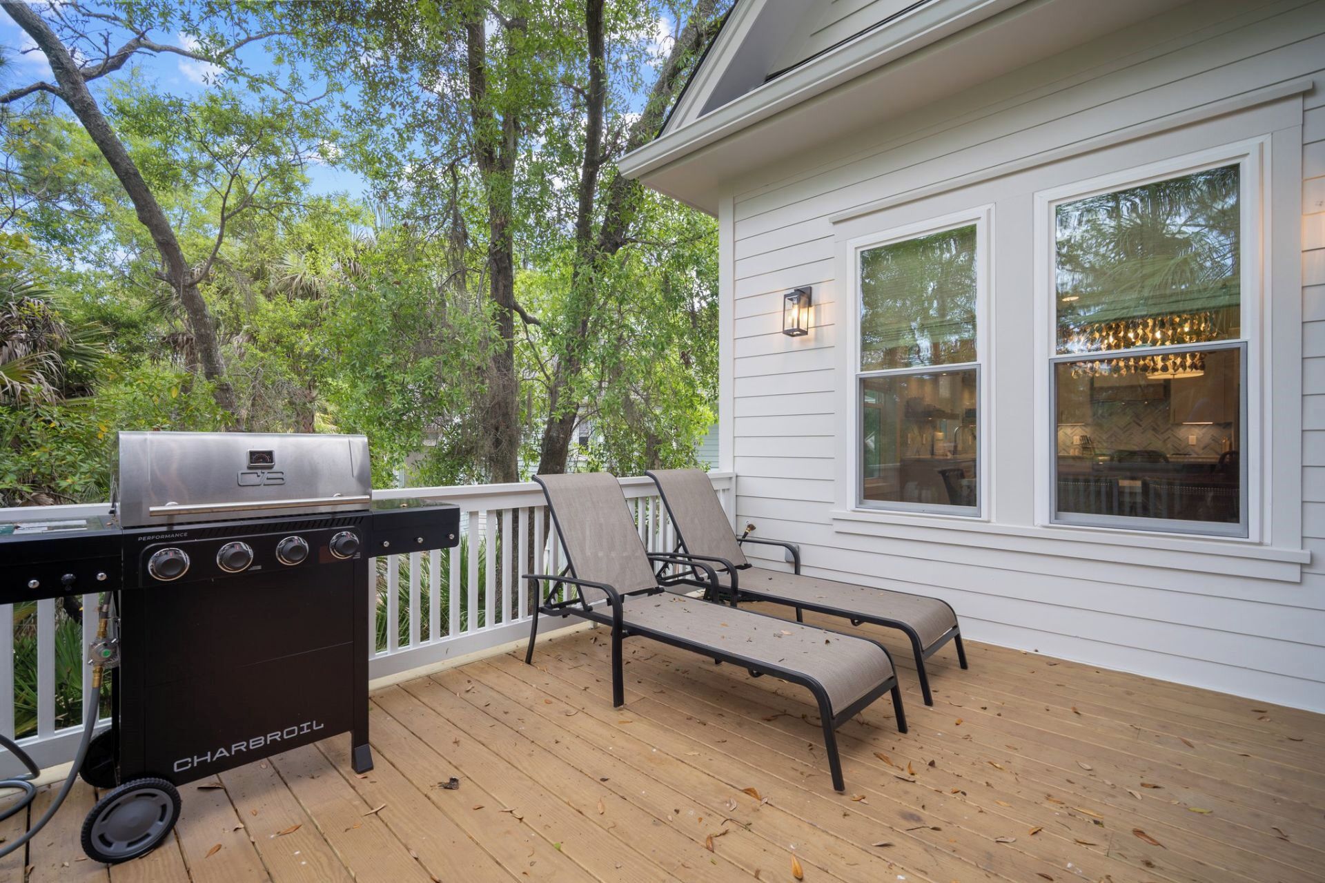A deck with a Charbroil grill, two lounge chairs, and a white house with large windows.