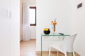 A modern room with a glass table, a white chair, a vase with flowers, and a window with curtains. - Acquamarina – Quadruple Room (Leverano)