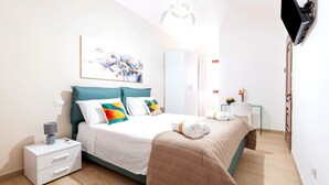 A modern bedroom with a bed, bedside tables, a nightstand, a wall-mounted lamp, and a painting. - Acquamarina – Quadruple Room (Leverano)