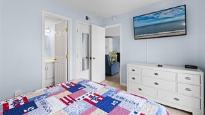 A bedroom with a bed, a dresser, a painting of a beach, and a door leading to another room. - Wight Bay 254 by Seaside Vacations & Sales (Ocean City)